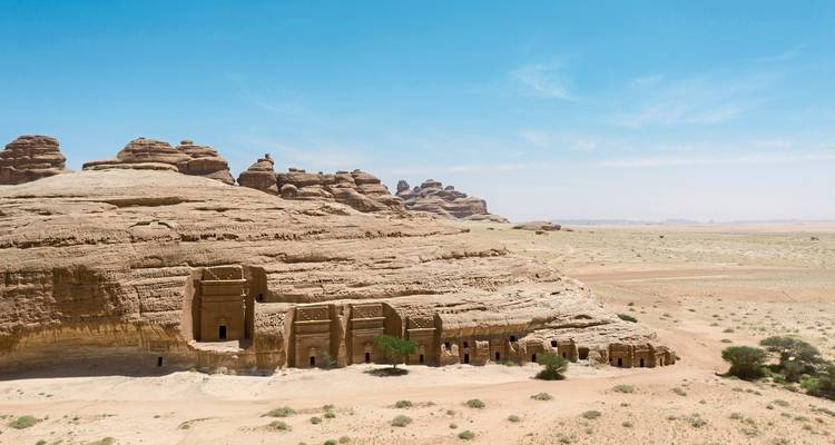 Series of rock-cut tombs within a desert landscape.