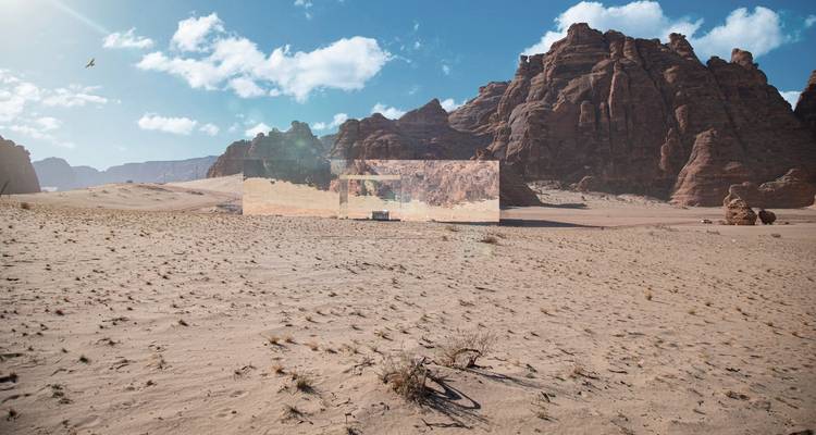 Large mirrored structure in a desert landscape with mountains.