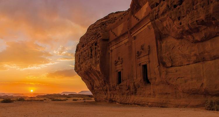 Old rock structure with carvings at sunset.