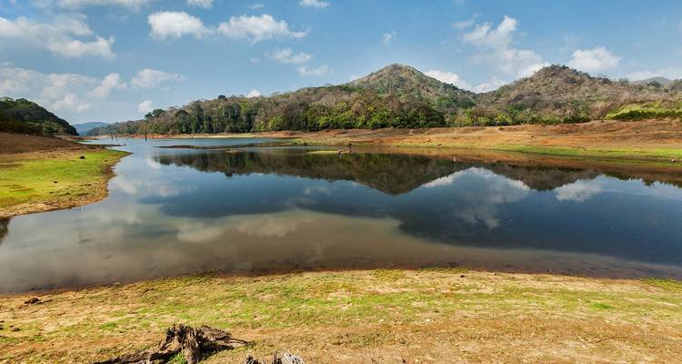 A calm lake reflects surrounding hills and scattered clouds in Periyar wildlife sanctuary.