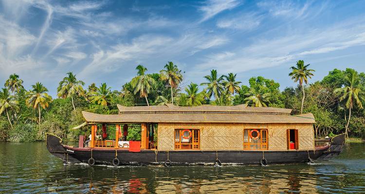 A traditional thatched-roof houseboat cruises along the lush palm-lined backwaters of Kerala.