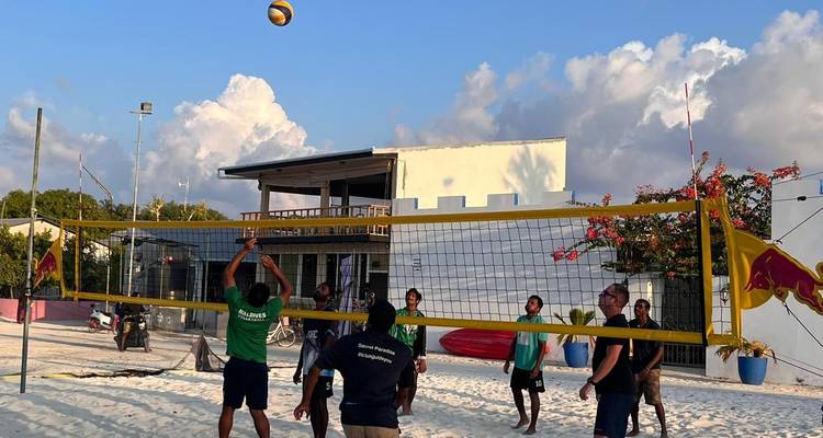Mensen die strandvolleybal spelen op wit zand voor een gastenverblijf onder een blauwe lucht