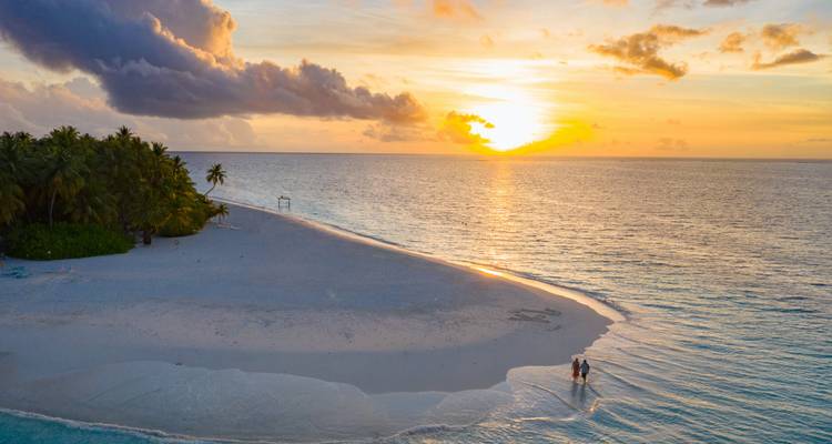 Couple walking along the beach at sunset.