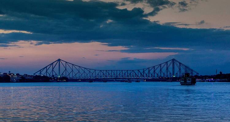 Silhouette du pont Howrah au crépuscule au-dessus d'une rivière calme.
