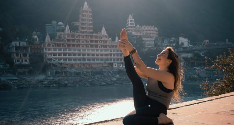 Femme pratiquant le yoga au bord de la rivière avec des temples en arrière-plan.