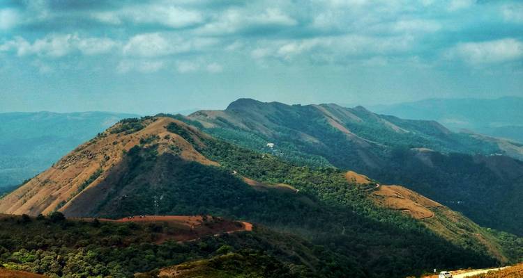 Une vue panoramique de collines ondulées et de forêts sous un ciel nuageux.