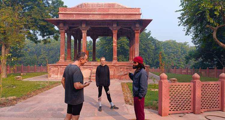 Three people chatting in front of a historic red sandstone structure.