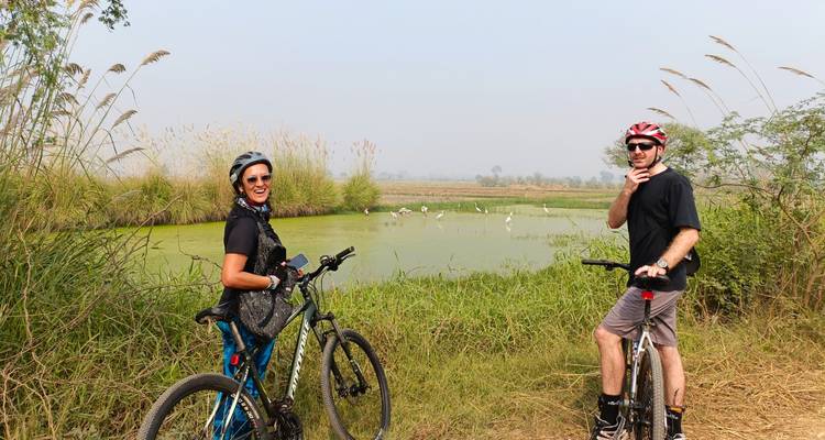 Two cyclists posing near a pond with birds.