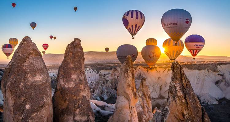 Hot air balloons floating over dramatic rock formations.