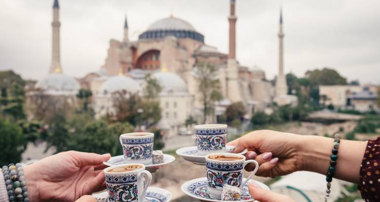 Handen heffen zich met sierlijke Turkse koffiekopjes terwijl de Hagia Sophia wazig op de achtergrond zichtbaar is.