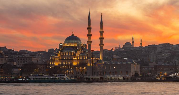 Verlichte moskee aan de Istanbul waterkant gloedt onder een vurige zonsonderganghemel.