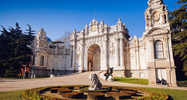 Sierlijke barokke poort van het Dolmabahce-paleis met verzorgde tuin en leeuwstandbeeld.