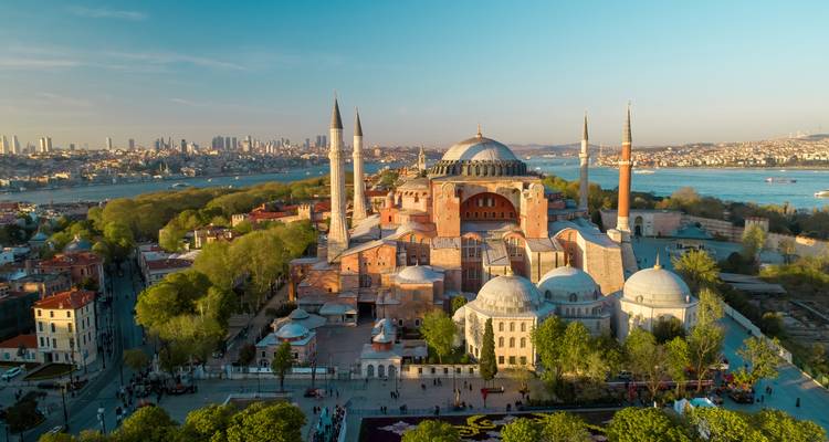 Drone-opname van de Hagia Sophia met haar minaretten, de Bosporus en de skyline van Istanbul in warm licht gehuld.