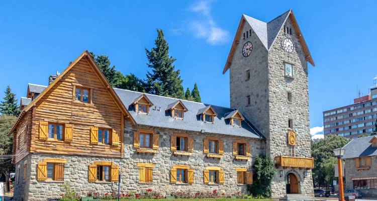 Edificio histórico de piedra con torre de reloj en un entorno soleado.