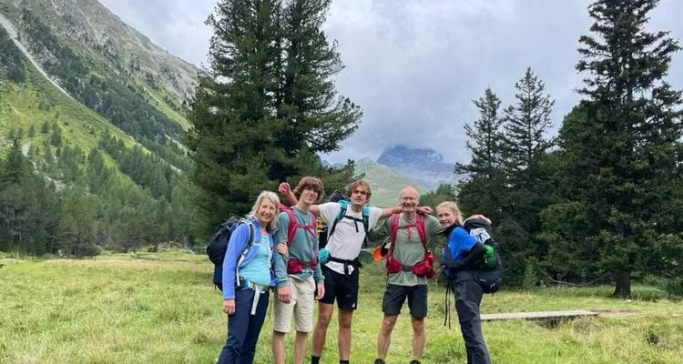 Groupe familial posant dans un pré alpin herbeux avec des sommets nuageux en arrière-plan.