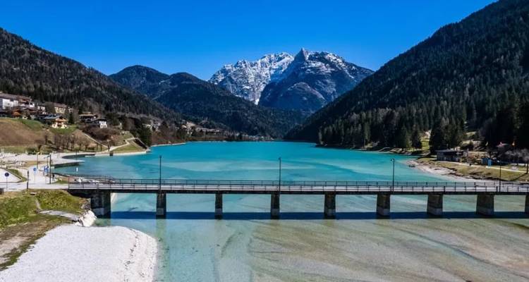Lac de montagne turquoise traversé par un pont avec des sommets enneigés au loin.