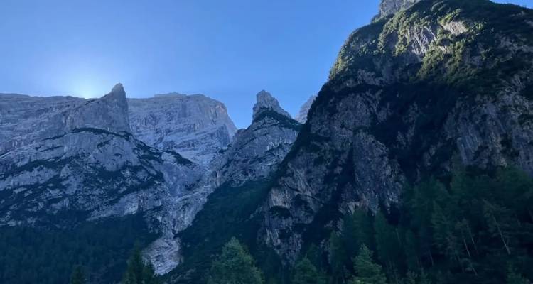 Falaises rocheuses escarpées et pentes boisées avec le soleil matinal derrière un pic rocheux.