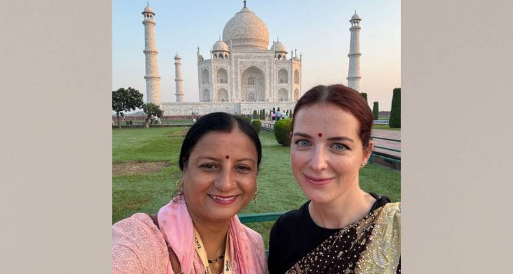 Two women in traditional attire posing in front of the Taj Mahal.