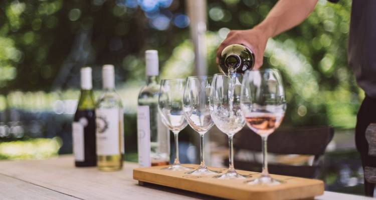 Person, die Wein in Gläser auf einem Holztisch eingießt.