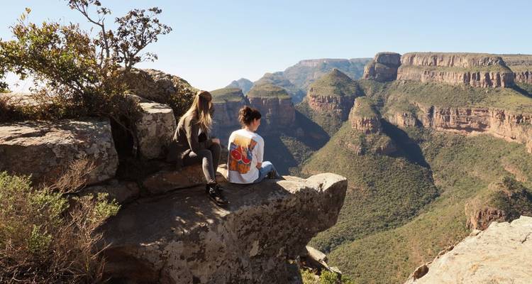 Zwei Menschen sitzen auf einem Felsen und blicken über eine weite Schlucht.