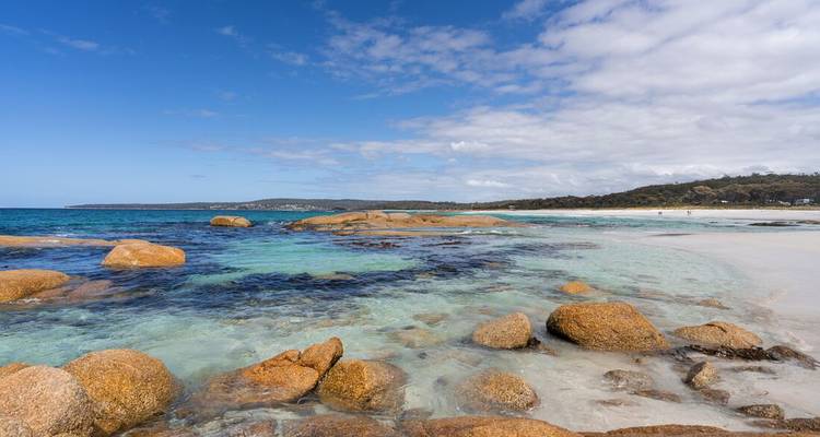 Eau turquoise cristalline et rochers couleur rouille sur une plage tasmanienne ensoleillée