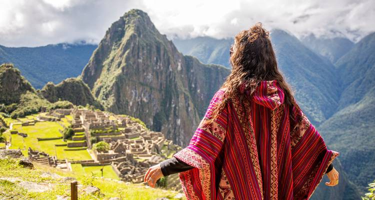 Person wearing a colorful poncho overlooking Machu Picchu with the iconic mountain in the background.