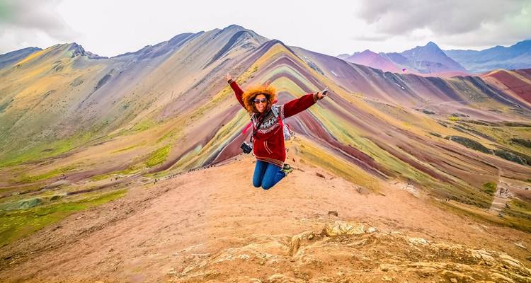 A person jumping joyfully with colorful mountain ridges behind.
