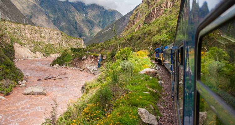 Train traveling through a lush valley alongside a river.