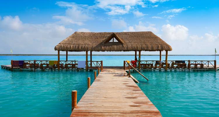 Wooden pier with a thatched roof structure on a blue lake.