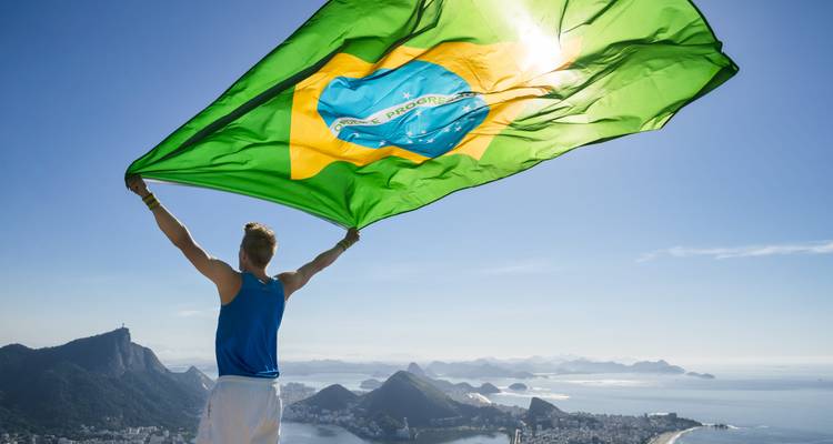 Persona sosteniendo una bandera brasileña con vista a las montañas de fondo.