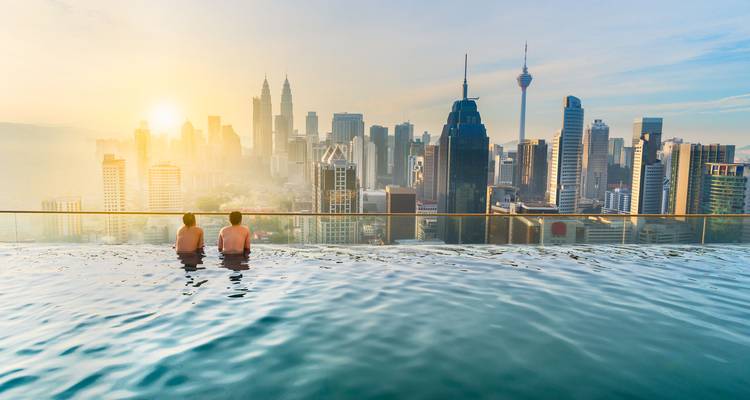 Deux personnes profitant d'une piscine à débordement avec vue sur le paysage urbain au coucher du soleil.
