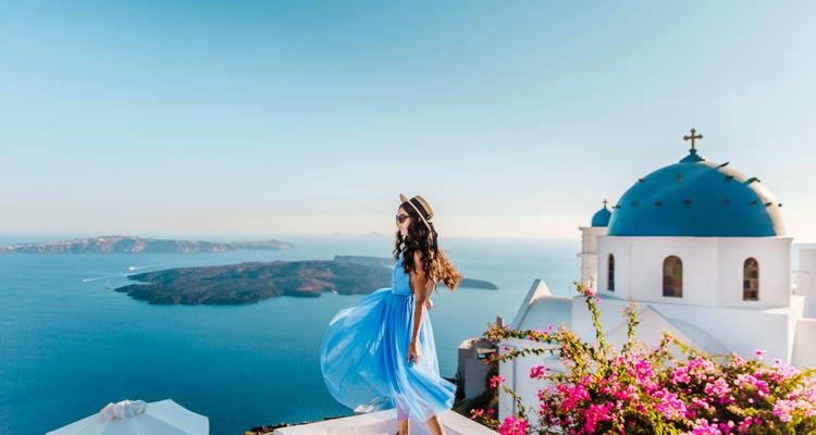 Woman in a blue dress overlooking the sea and buildings with blue domes, likely in Santorini.