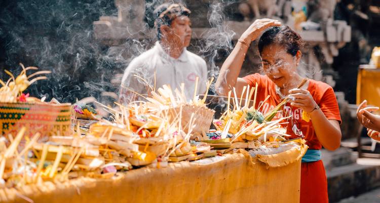 Offrandes balinaises traditionnelles sur une table avec des personnes effectuant des rituels.