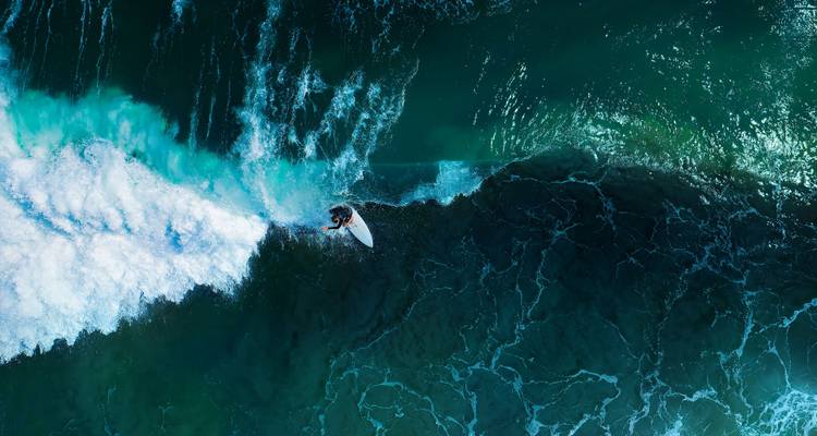 Vue aérienne d'un surfeur sur une vague d'un bleu éclatant.