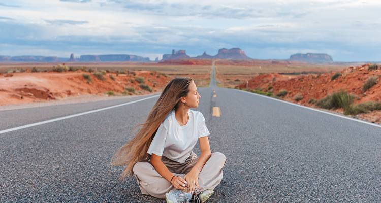 Persona sentada en una carretera del desierto con formaciones rocosas pintorescas.