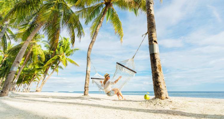Persona relajándose en una hamaca entre palmeras en una playa de arena.