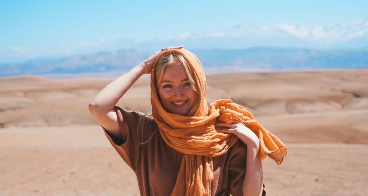 Lächelnde Person mit Schal um den Kopf in Wüstenlandschaft.