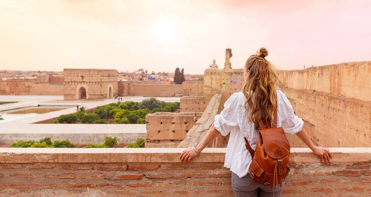 Person mit Rucksack blickt bei Sonnenuntergang über antike Ruinen.