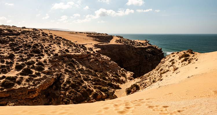 Sandy coastal dunes with a clear blue sky and ocean view.