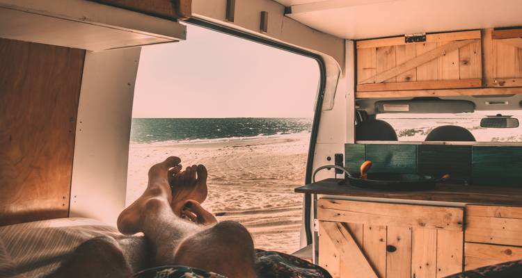 Person entspannt sich in einem Wohnmobil mit Blick auf den Strand vor der offenen Tür.