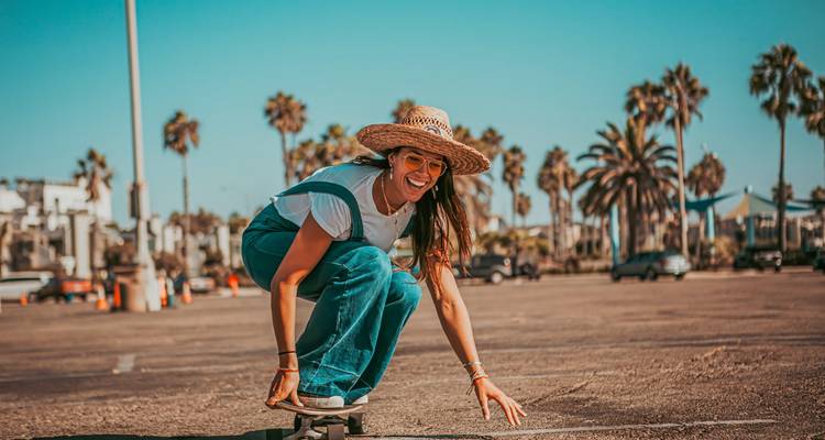 Person beim Skateboarden in einem sonnigen Bereich mit Palmen.
