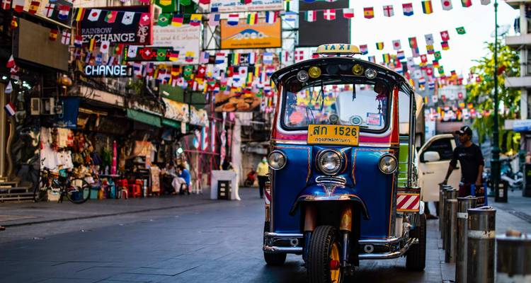 Tuk-Tuk in einer bunten, belebten Straße voller Fahnen und Schilder.
