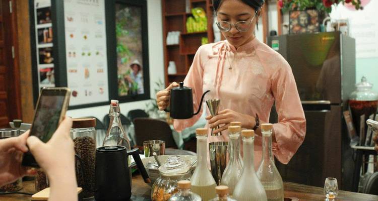 Femme dans un café préparant du café avec divers ingrédients visibles.
