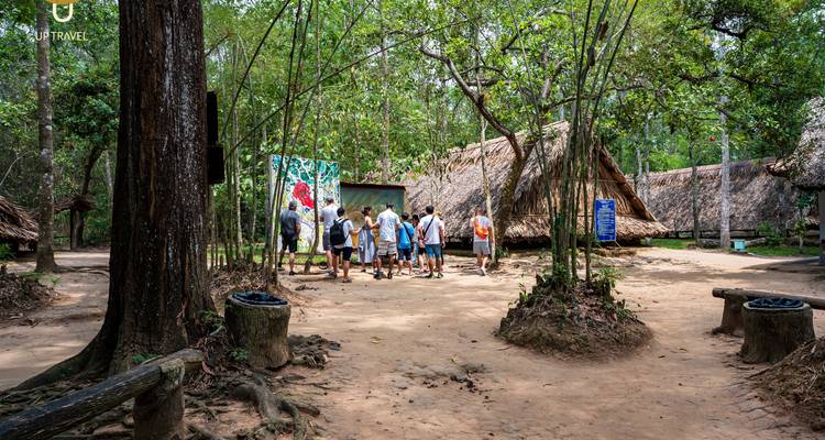 Tourists exploring Cu Chi Tunnel area with huts and surrounding forest.