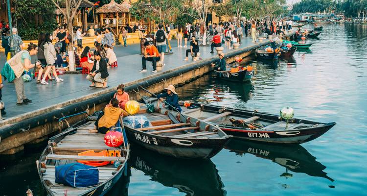 Busy market area with boats and people along a river.