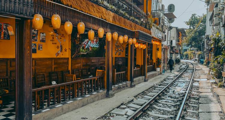 Rue étroite avec des cafés et des lanternes le long d'une voie ferrée.