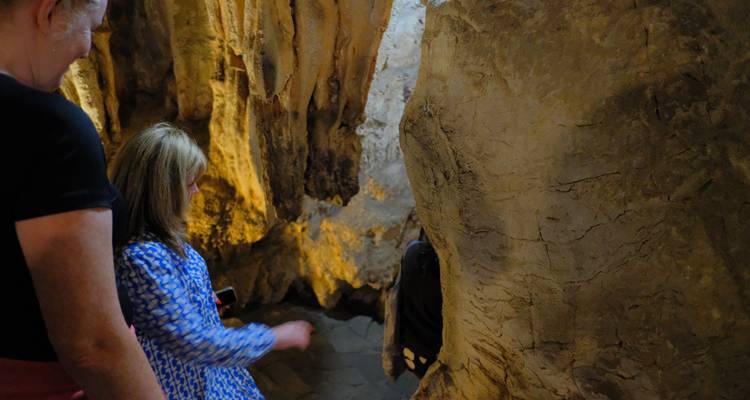 Touristes explorant une grotte faiblement éclairée avec des stalactites et des stalagmites.