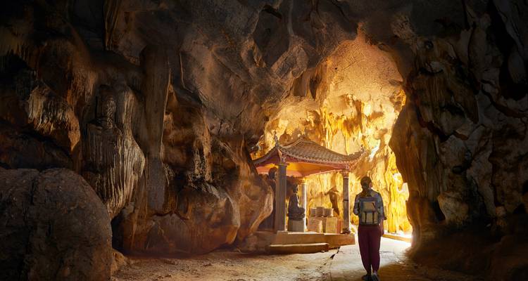 Une personne marchant à l'intérieur d'une grotte avec un petit sanctuaire.
