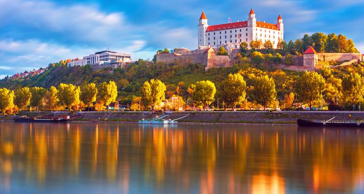 Castle on a hill reflected in a river during sunset.