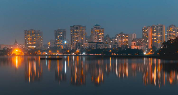 El horizonte de la ciudad al atardecer reflejado en un lago tranquilo con luces cálidas brillando.